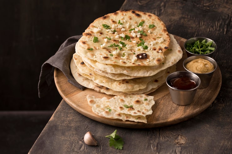 A soft, white jowar roti puffed up fresh on a hot tawa, held gently with metal tongs over a low gas flame.
