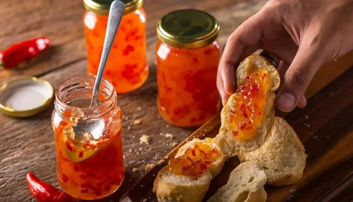A gourmet cheeseboard featuring a jar of vibrant red chili-infused fruit jam surrounded by cheese and crackers.